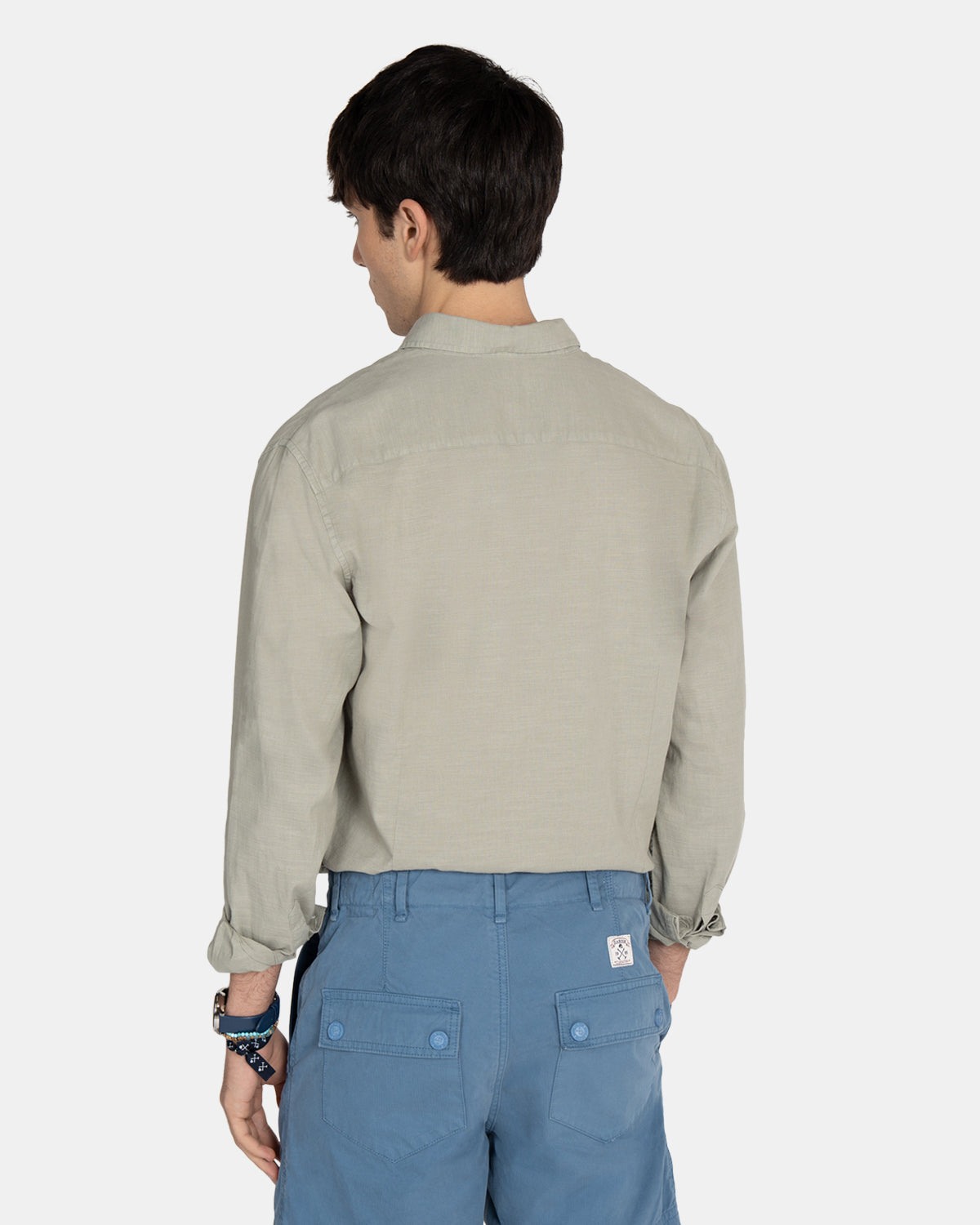 Vista trasera del modelo con camisa Royal Academy en verde gris remangada sobre bermudas azules