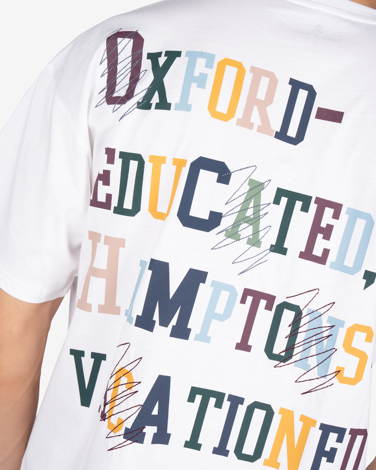 Detalle del mensaje multicolor Oxford-educated con tachones bordados en la camiseta LIVERPOOL blanca