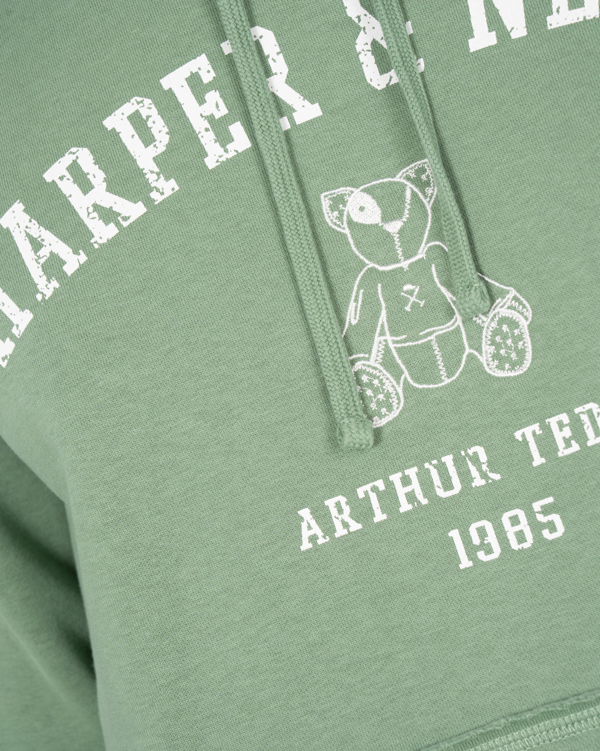 Detalle del estampado Harper Neyer arqueado en efecto vintage y osito Arthur Teddy bordado en la sudadera MANCHESTER verde salvia
