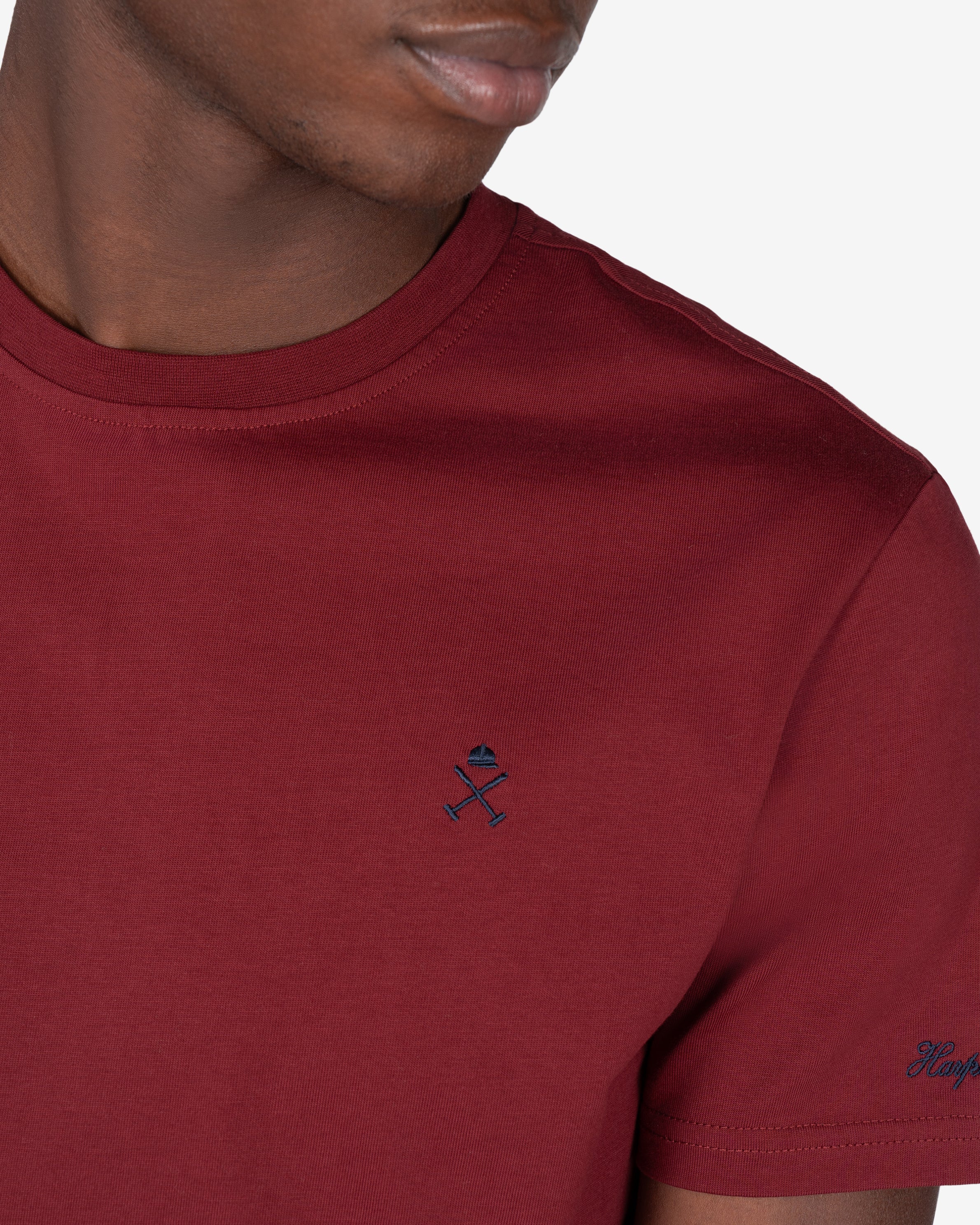 Detalle del logo bordado en azul marino sobre burdeos de la camiseta PARADISE de Harper & Neyer