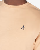 Detalle del logo bordado en azul marino sobre camel de la camiseta PARADISE de Harper & Neyer