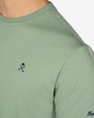 Detalle del logo bordado en azul marino sobre verde salvia de la camiseta PARADISE de Harper & Neyer