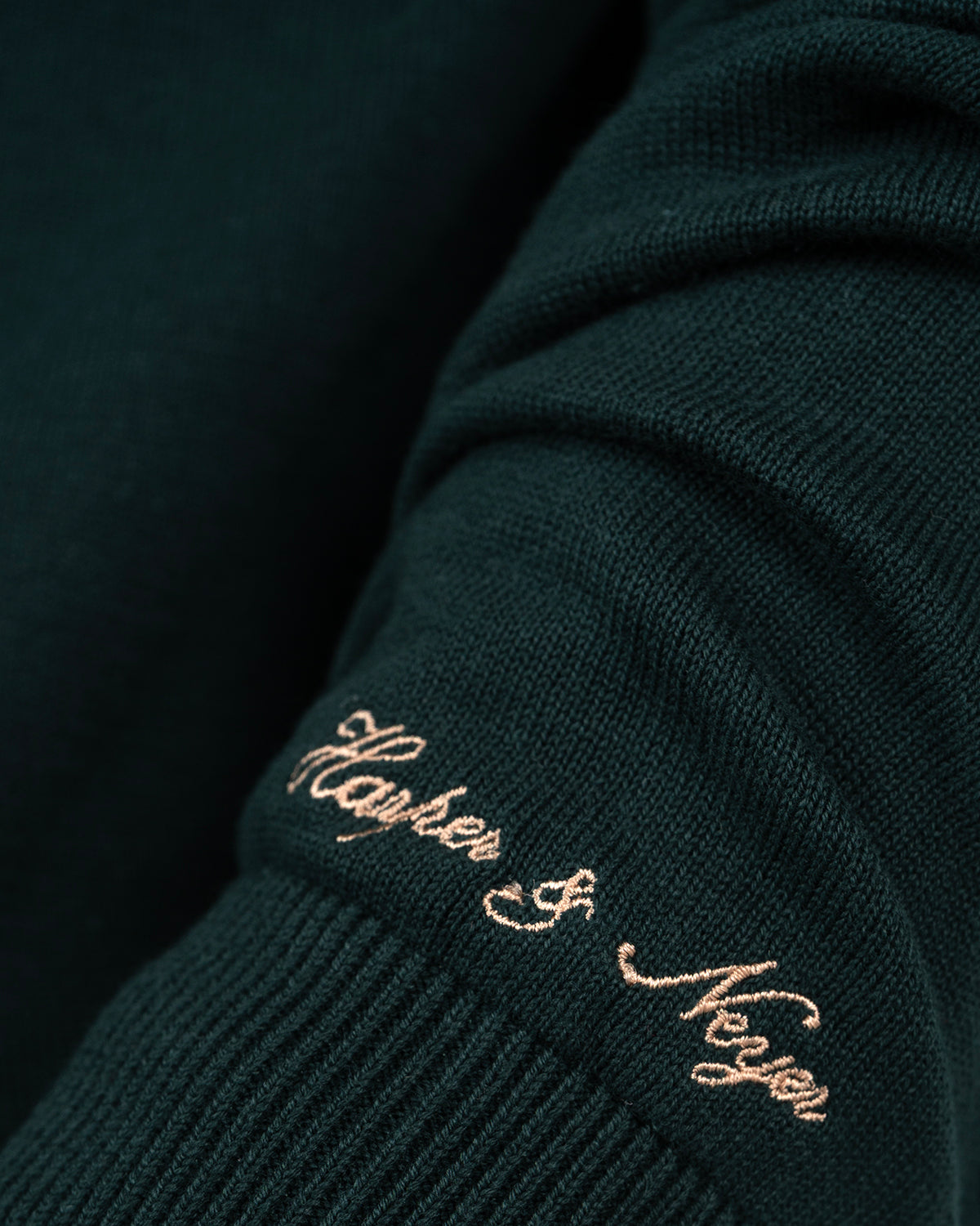 Detalle de la firma Neyer bordada en camel en el puño del jersey ICON verde botella de Harper & Neyer