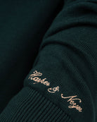 Detalle de la firma Neyer bordada en camel en el puño del jersey ICON verde botella de Harper & Neyer