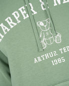 Detalle del estampado Harper Neyer arqueado en efecto vintage y osito Arthur Teddy bordado en la sudadera MANCHESTER verde salvia