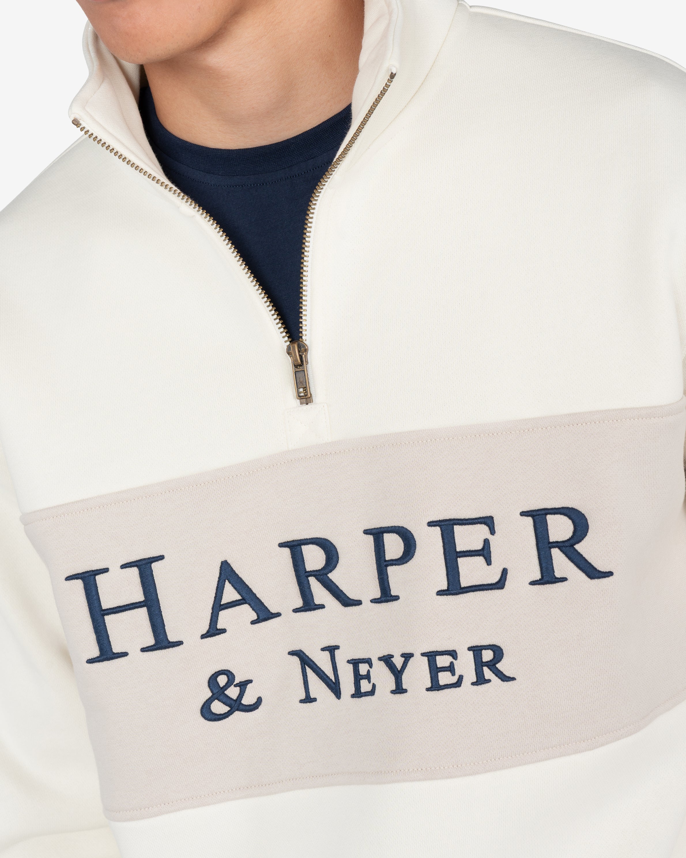 Detalle de la media cremallera dorada y logo Harper Neyer bordado en azul marino sobre panel beige de la sudadera MARYLAND