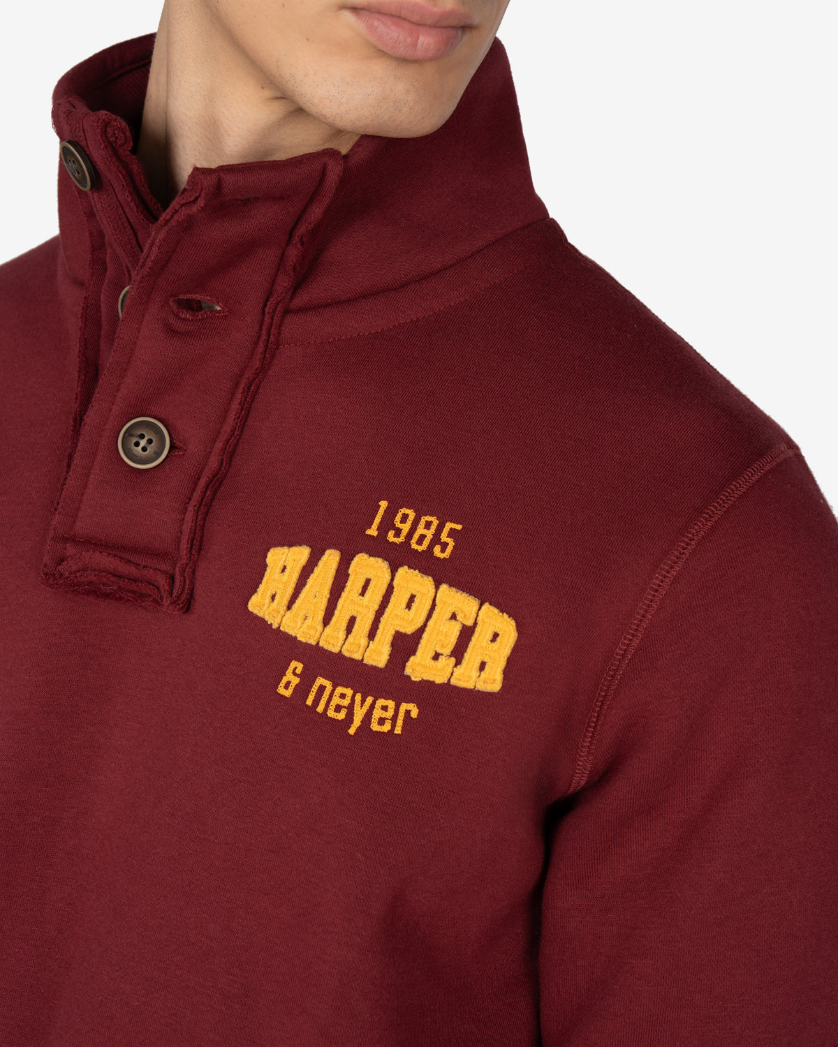 Detalle de la tapeta de tres botones con bordes deshilachados y bordado 1985 Harper Neyer en amarillo mostaza de la sudadera RAVENS burdeos