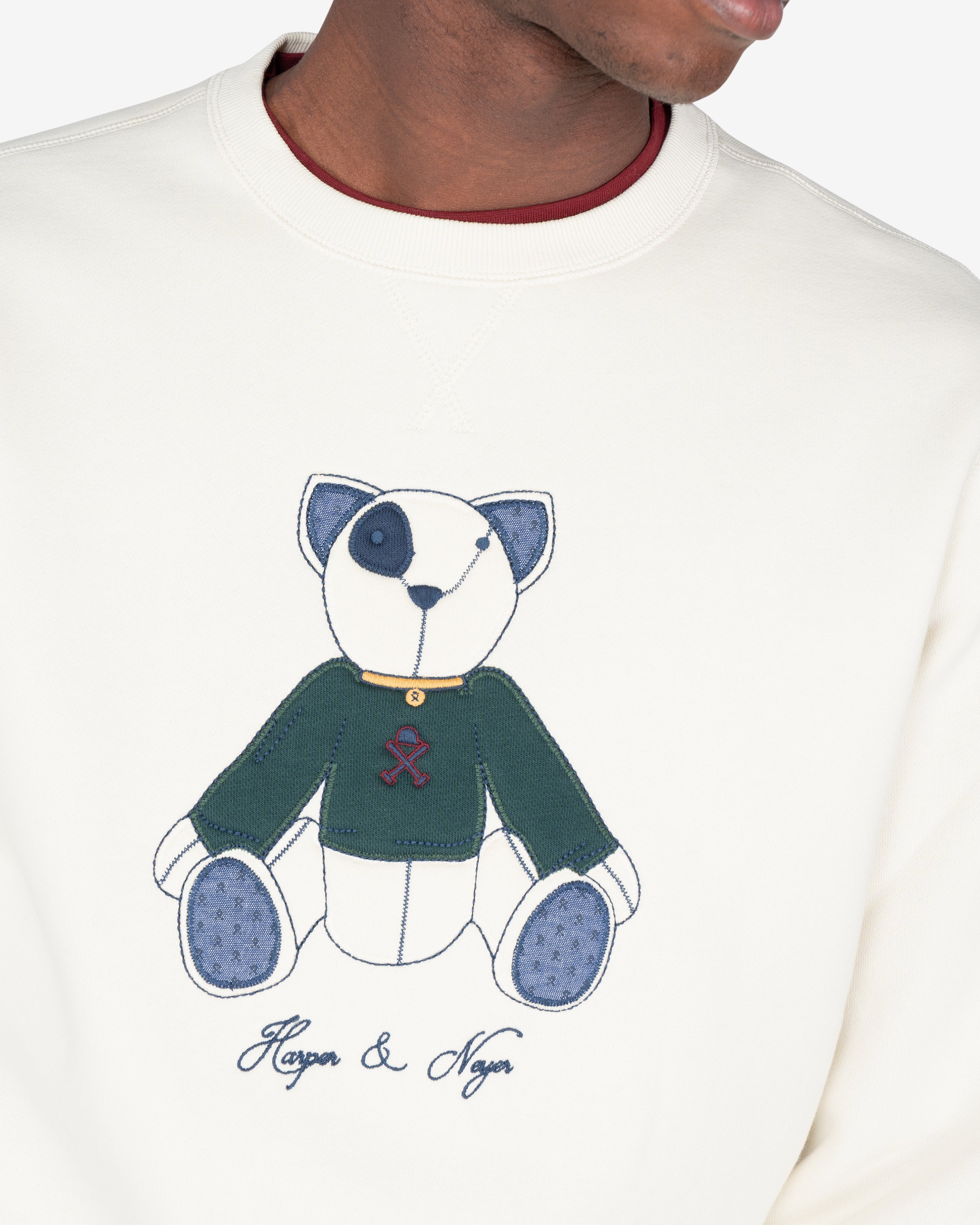 Detalle del oso Teddy en appliqué con blanket stitch, jersey verde botella y logo Harper & Neyer en burdeos